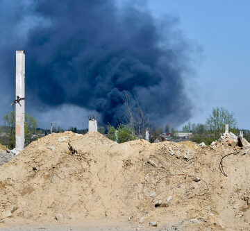 A,Pile,Of,Concrete,Rubble,With,Protruding,Rebar,On,The A pile of rubble with dark smoke in the distance