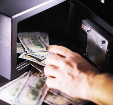 Hand Putting Money Into Steel Safe