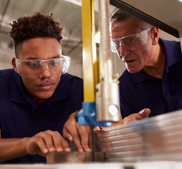 Carpenter Training Male Apprentice To Use Mechanized Saw