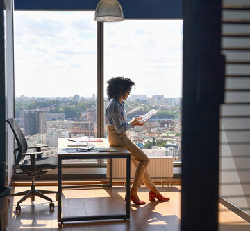 Young,Successful,Female,African,American,Executive,Manager,Ceo,Sitting,On Female CEO sitting on edge of desk in office building