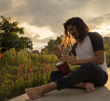 Man With Long Hair Playing The Drum In The Park