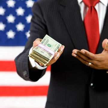 Politician Gesturing to Stack of U.S. Currency