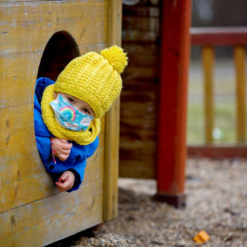 Young child, with face mask, playing on a playground.
