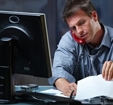 Mid-adult,Businessman,Speaking,On,Landline,Phone,Working,Overtime,In,Office Businessman Speaking On Landline Phone Working In Office