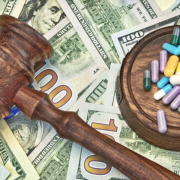 A Wooden Gavel and Colorful Pills On Top Of Scattered U.S. Currency