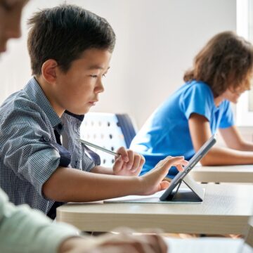 Focused,Asian,School,Boy,Using,Digital,Tablet,At,Class,In SCHOOLS SURRENDER TO AI