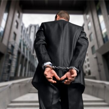 Handcuffed Businessman Being Led Away Between Office Buildings