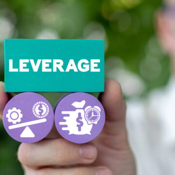 Man's Hand Holding Block With Leverage Balanced Over Financial Scale And Business Earnings