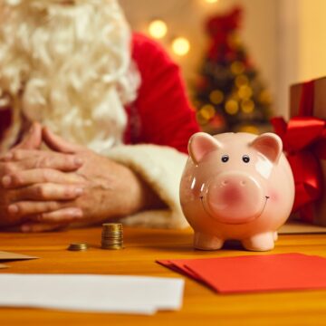 Close-up Of Piggy Bank On Desk With Presents And Santa