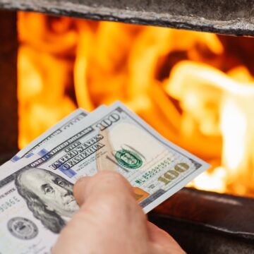 Throwing Dollar Bills Into The Fire Symbolizing Spending/Wasting A Lot Of Money