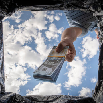 Hand Throwing Away Dollars Into A Trashcan