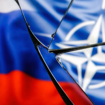 The Flags Of Russia And NATO Behind Broken Glass