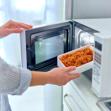 Female Hands Putting A Container Of Food Into The Microwave