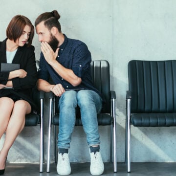 Man Whispering To A Woman In An Office Reception