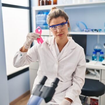 Young,Woman,Working,At,Scientist,Laboratory,Holding,Pink,Ribbon,Thinking RESEARCHERS TAME ROGUE PROTEIN IMPLICATED IN 75 PERCENT OF ALL CANCERS
