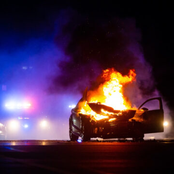Car On Fire At Night With Police Lights In Background