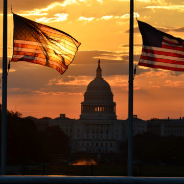 United States Capitol Building Silhouette And U.S. Flags At Sunrise