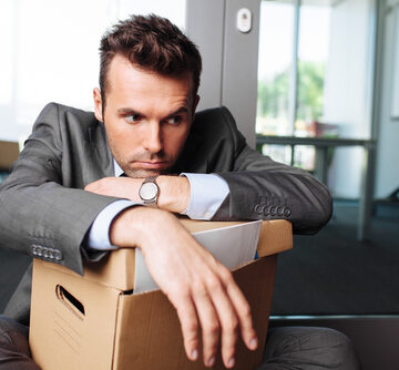 Young Laid Off Office Worker Sitting Down With A Carton Of Office Belongings