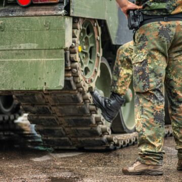 Two,Soldiers,In,Camouflage,Uniform,Standing,During,A,Break,Under Two Soldiers In Camouflage Uniform Standing Next To A Tank