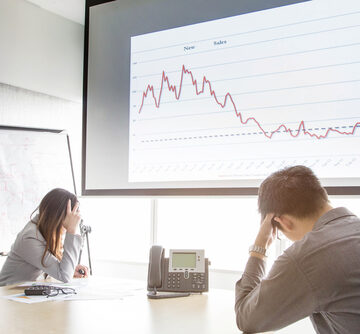 Man And Woman In Meeting Room Holding Their Heads While Viewing A Slide Projection With A Down Arrow