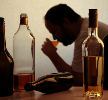 Silhouette Of Anonymous Alcoholic Person Drinking Behind Bottles Of Alcohol