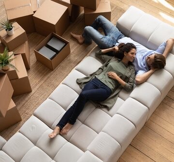 Overhead View Of Young Couple Resting On Couch Next To Moving Boxes