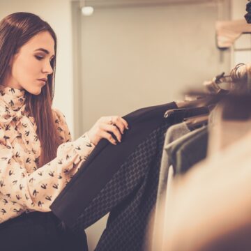 Young Woman Choosing Clothing On A Clothes Rack In A Showroom