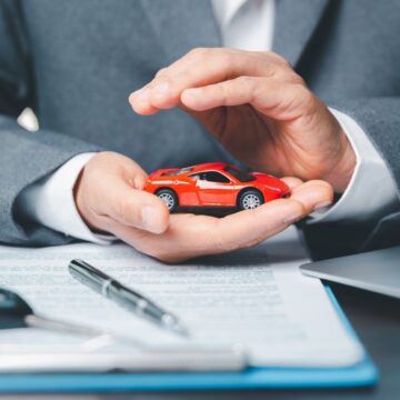 Business,Woman's,Hand,Protecting,Red,Toy,Car,On,Desk.,Planning Businessperson's Hand Protectively Holding Small Red Toy Car