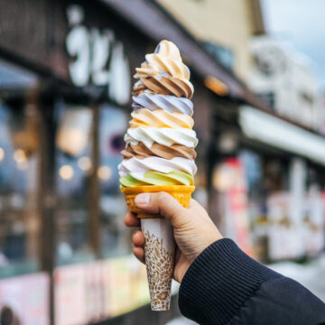 A Hand Holding A Tall, Mixed, And Colorful Stack Of Soft Ice Cream In A Cone