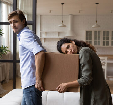 Tired, Millennial Spouses Carrying Heavy Moving Box