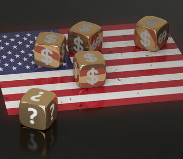 Gold Dice With Dollar Signs And Question MArks Sitting Atop A U.S. Flag