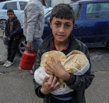 Palestinian Boy Holds Armful Of Bread As Crowd Receives Food Supplies At A UNRWA School