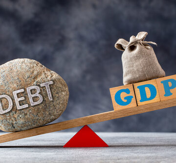 Debt-to-GDP Ratio Illustrated With A Large Stone With The Word Debt And A Wooden Block With GDP Balancing On A See-Saw