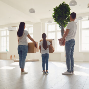 Young Family Of Three Moving With Boxes Into A New Home