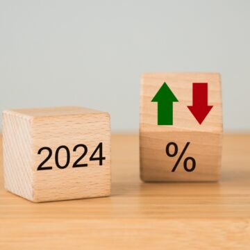 Two Wooden Cubes With The Year 2024 On One, A Percentage Sign Plus Up And Down Arrows On The Other