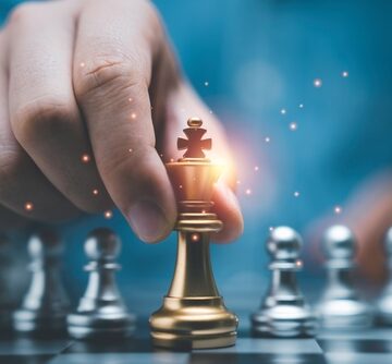 Businessman,Holding,Golden,King,Chess,In,Front,Of,Silver,Pawn Man's Hand Holding Golden King Chess Piece In Front Of Silver Pawn