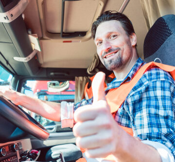 Smiling Truck Driver Sitting In Truck Cab Giving Thumbs-up
