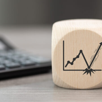 Wooden Cube With Erratic Stock Graph On Side And Keyboard In Background
