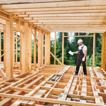 Worker Building Wooden Frame For Two-story House In The Woods