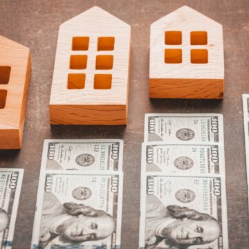 Image Of Different Sized Wooden Houses With Varying Stacks Of U.S. Currency