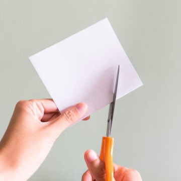 Person Cutting White Paper With Scissors