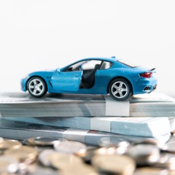 Concept Of Securing Car Loan With Model Sportscar Atop Stacks Of Bills And Pile of Coins