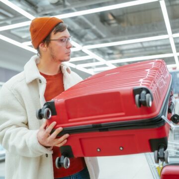 Man In A Store Contemplating The Purchase Of A Red Hardshell Suitcase