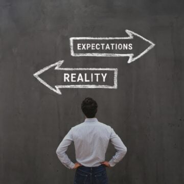 Concept Image Of Man Deciding Between The Words Reality Versus Expectation Written On A Blackboard