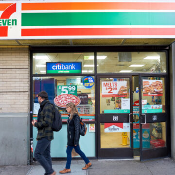 A Couple Walking By The Exterior Of A 7-Eleven Shop In New York,NY