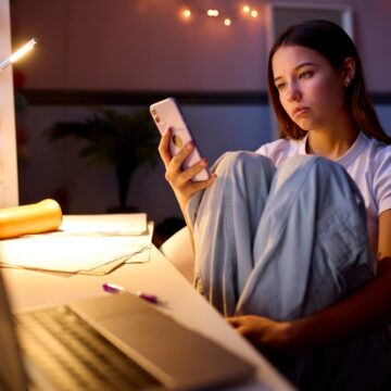 Unhappy Teenage Girl Sitting At Her Desk Scrolling On Mobile Phone