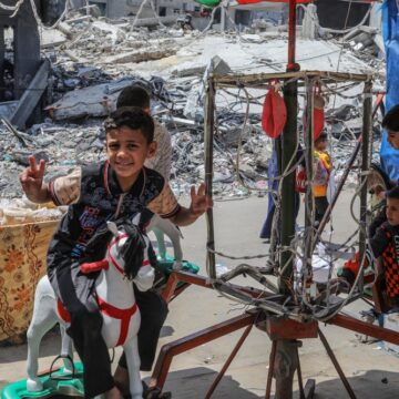 Displaced Palestinian Children Play On A Merry-go-Round Amid Rubble From Airstrikes