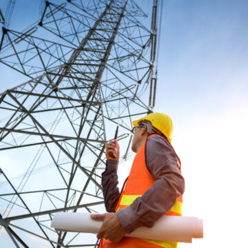Construction Worker Checking Site Near High Voltage Tower