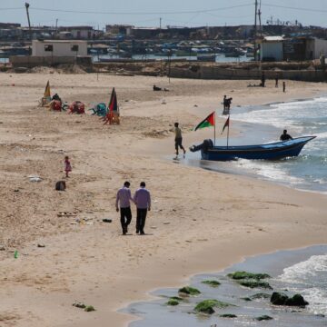 Palestinians Walk On A Beach With Small Boat On A Sunny Day
