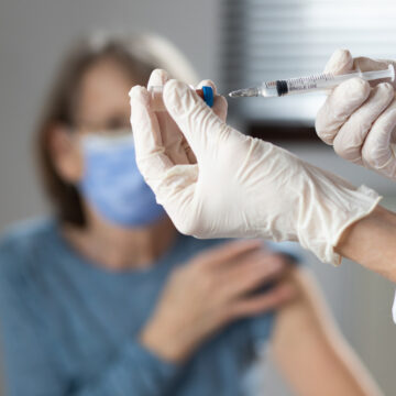 Elderly, Masked Woman Rolling Up Her Sleeve To Get A Coronavirus Vaccine Shot